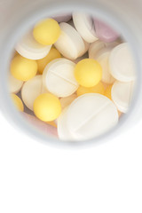 medicines various tablets and capsules  on a white  background with  container in blur on behind