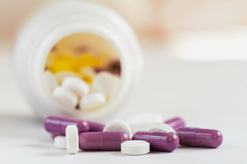 medicines various tablets and capsules  on a white  background with  container in blur on behind