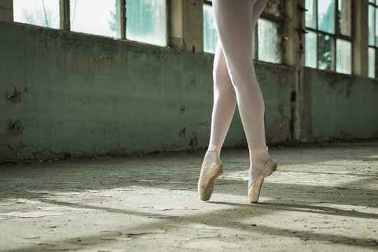 Photo of ballerinas toe walking in an old building, rustic surrounding.