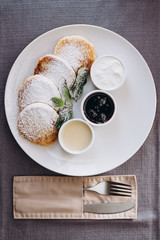 Delicious and hearty dessert, home made cottage cheese fried in a pan and served with sauces. Cheesecake, fresh jam and mint. Cottage cheese pancakes or curd fritters decorated powdered sugar in plate