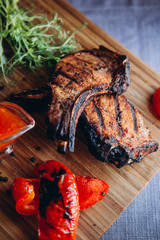 two appetizing pieces of fried ribs served on a wooden board with greens, and grilled vegetables