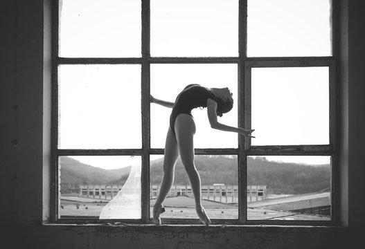 Black and white photo of ballerina in the window frame in an old building.