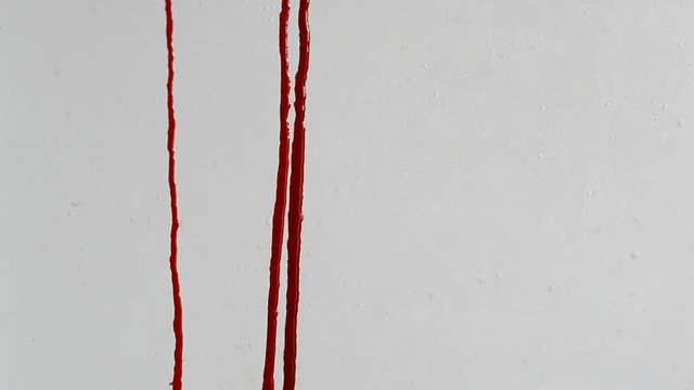 Trickles of blood flow down the white wall close-up. Creepy abstract background. Concept of a horror film or murder