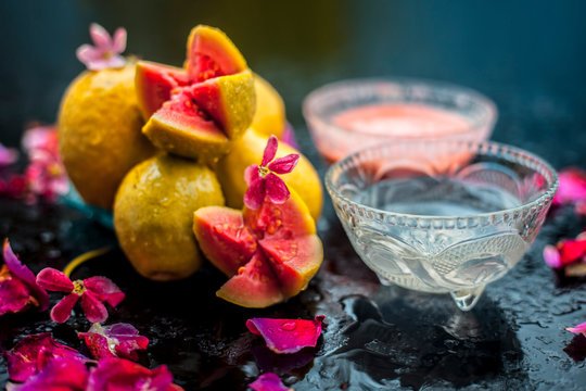Guava pulp and water well mixed in a glass bowl on the wooden surface along with some raw cut guava, with some rose petals, also completing a face mask used for a natural glow.