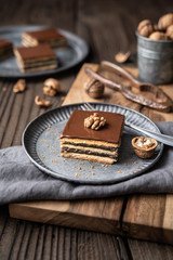 Fototapeta na wymiar Gerbeaud bars filled with plum marmalade and crushed walnuts, topped with chocolate frosting on wooden background