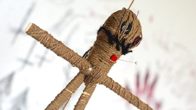 Voodoo doll with needles turns round slowly on white background with creepy ritual symbols. Dark magic and halloween concept