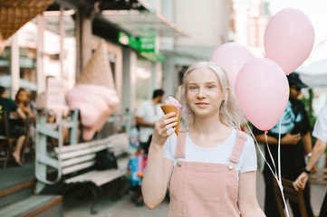Portrait teenager girl with blond hair and ice cream in her hand,holds inflatable balls in her hands,looks into the camera and smiles.Lovely lady with ice cream and balloons in their hands to walk