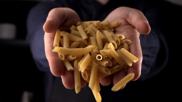 Penne pasta falling from man's hands on dark background, cooking in slow motion