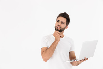 Image of unshaven thinking man holding laptop and looking upward at copyspace