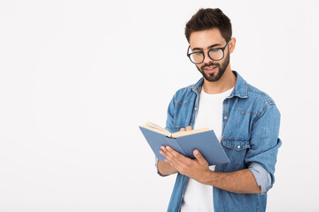 Image of young smart man wearing eyeglasses holding and reading book - obrazy, fototapety, plakaty