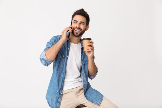 Image of handsome smiling man drinking coffee takeaway and talking on cellphone while sitting