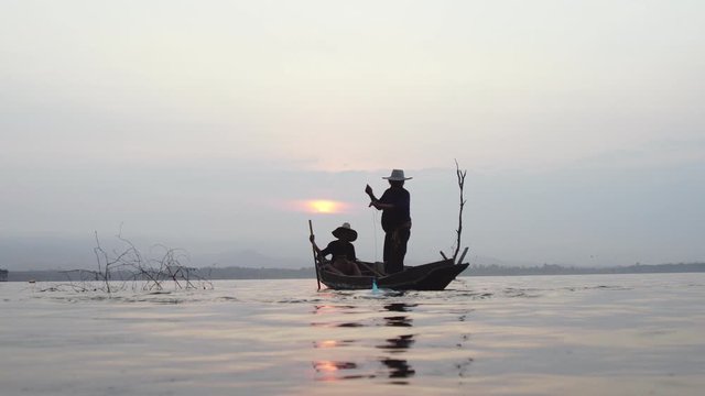 Silhouette of traditional fisherman and his son hunting fish together. The fisherman throwing net in the lake at sunrise time