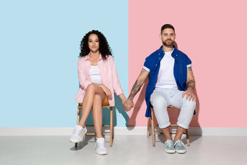Naklejka premium Young emotional caucasian couple in bright casual clothes posing on pink and blue background. Concept of human emotions, facial expession, relations, ad. Woman and man holding hands, look happy.