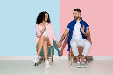Obraz premium Young emotional caucasian couple in bright casual clothes posing on pink and blue background. Concept of human emotions, facial expession, relations, ad. Woman and man holding hands, look happy.