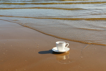 Fototapeta na wymiar A cup of coffee stands on the sandy seashore