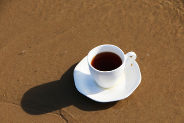 A cup of coffee stands on the sandy seashore