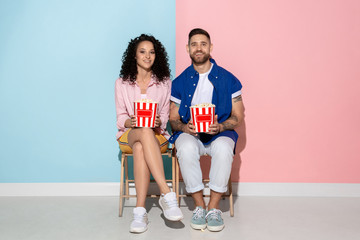 Young emotional caucasian couple in bright casual clothes posing on pink and blue background. Concept of human emotions, facial expession, relations, ad. Woman and man watching TV with popcorn.