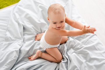 Top view of baby in diaper sitting on bed and clapping hands
