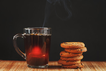 Oatmeal cookies with chocolate pieces and a mug of aromatic black tea in on a bamboo substrate, Low contrast.