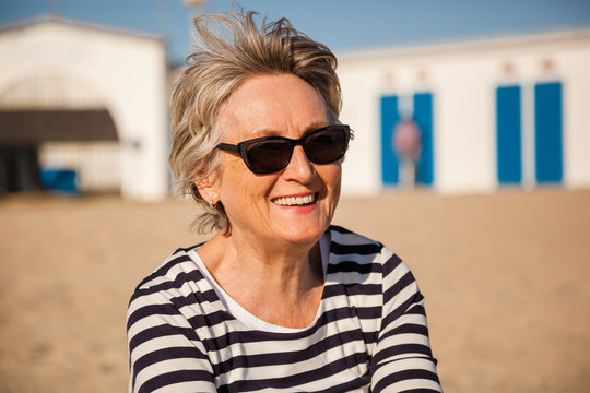 Natural portrait of active senior woman with sunglasses sitting on the beach