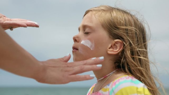 Mother applying sunscreen on the face of her daughter while at the beach on summer vacation.