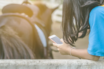 Girl in yellow and blue shirt use smartphone to take photos at the horse riding field in the...