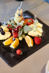 Fruit sliced on a stylish plate. Pineapple, pear, orange, apple, grape, wild strawberry.