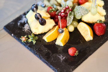 Fruit sliced on a stylish plate. Pineapple, pear, orange, apple, grape, wild strawberry.