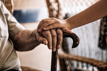 child's hand over old man's hand holding a cane. - Powered by Adobe