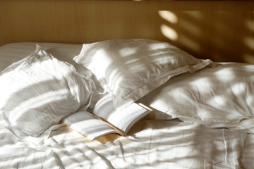 Bedroom scene with bedding and an open book bathed in morning light.