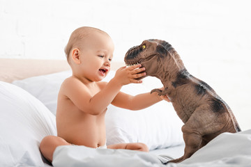 Little child sitting on white bed and holding toy dinosaur with both hands