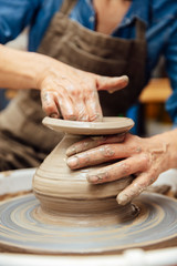 Senior female potter working on pottery wheel while sitting  in her workshop