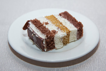 Close-up shot. Free space for text.Slice of chocolate cake white cream on plate. Chocolate cake with whipped cream . A slice of cake in a white plate on a white wooden table with a spoon.