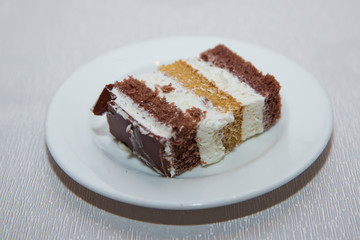 Close-up shot. Free space for text.Slice of chocolate cake white cream on plate. Chocolate cake with whipped cream . A slice of cake in a white plate on a white wooden table with a spoon.