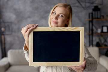 Girl holds a chalk board in the apartment. Copy space.