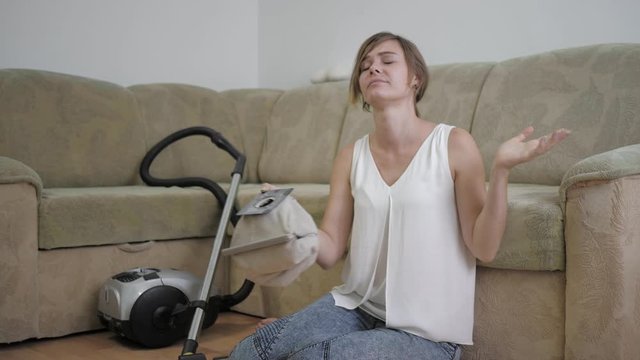 allergy to hygiene, a woman sitting on floor sneezes due to dust after cleaning room with a vacuum cleaner