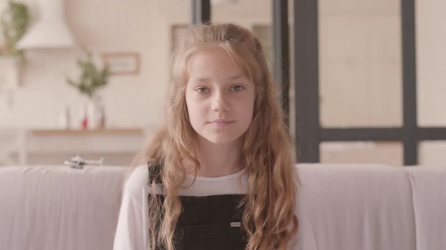 Portrait of cute fun teen girl dancing sitting on the couch and looking at the camera at home. Leisure indoors.