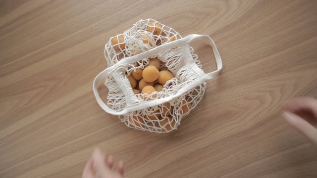 Hand put on mesh organic string bag with fruits on wooden table.ECO, zero waste
