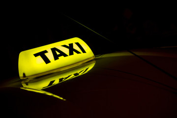 yellow taxi sign on the roof of cab at night