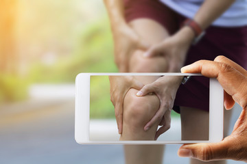 Doctor hand used smart phone take photo of Asian woman use hands hold on her knee injury while running .