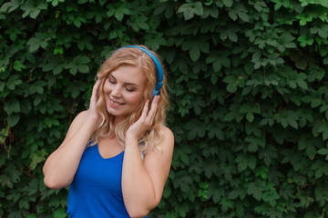 Beautiful young blonde girl in a dress listening to music in blue headphones. Real life, enjoy the moments. Copy space.