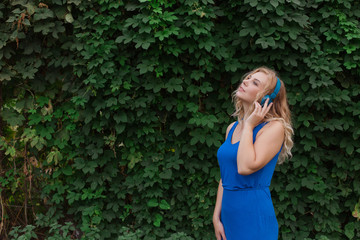 Beautiful young blonde girl in a dress listening to music in blue headphones. Real life, enjoy the moments. Copy space.