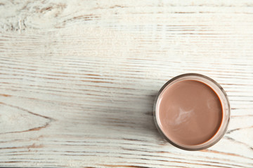 Glass of tasty chocolate milk on wooden background, top view with space for text. Dairy drink