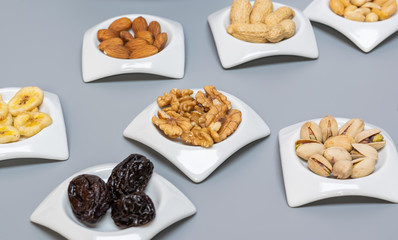 Food,taste and snack concept: nuts and dried fruits in white saucers on gray matte background,selective focus.