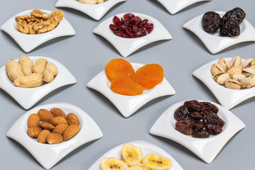 Food,taste and snack concept: nuts and dried fruits in white saucers on gray matte background,selective focus.