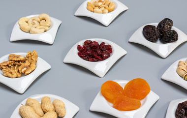 Food,taste and snack concept: nuts and dried fruits in white saucers on gray matte background,selective focus.