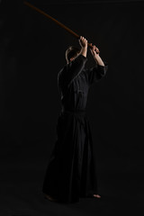 Kendo guru wearing in a traditional japanese kimono is practicing martial art with the shinai bamboo sword against a black studio background.