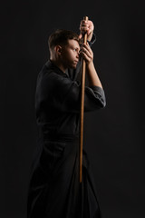 Kendo guru wearing in a traditional japanese kimono is practicing martial art with the shinai bamboo sword against a black studio background.