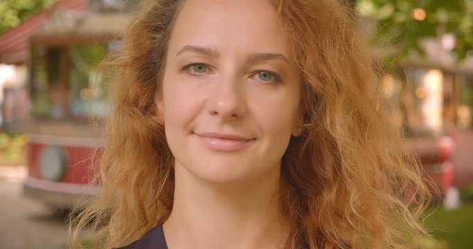 Closeup portrait of adult attractive redhead female looking at camera smiling happily in park outdoors