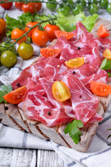Thin slices of Italian cold cut pork Coppa and cut cherry tomatoes on wooden board